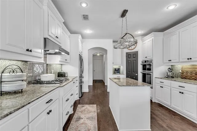 a large kitchen with stainless steel appliances granite countertop a stove a sink dishwasher and white cabinets with wooden floor