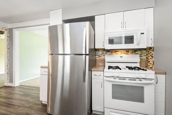 a kitchen with a sink dishwasher a stove and white cabinets with wooden floor