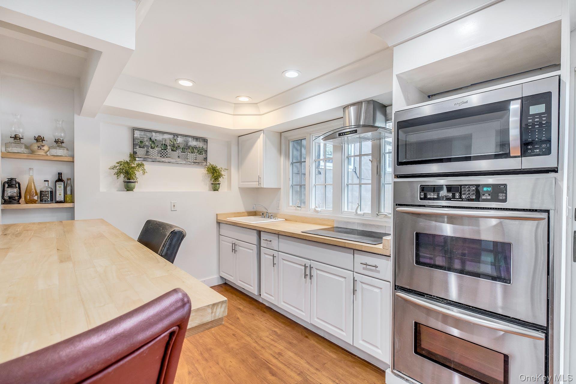 7 George Street Hampton Bays, NY 11946 - Photo 6 of 11 Kitchen featuring stainless steel built-in double oven and microwave, light wood-finish countertops, white cabinetry, and wood-finish flooring