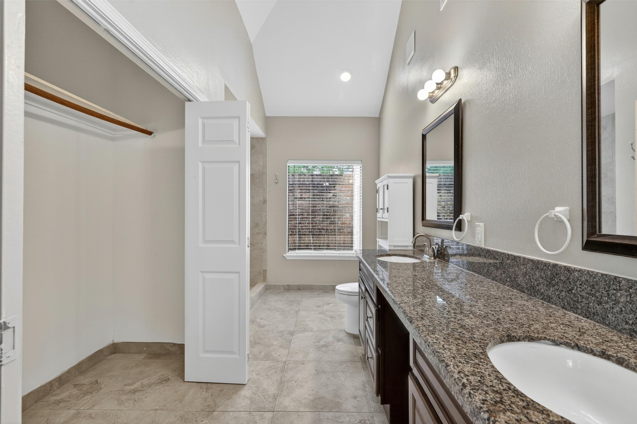 12929 Kingsbridge Lane Houston, TX 77077 - Photo 22 of 42 Spacious spa-inspired primary bathroom featuring an oversized vanity with granite countertops, elegant cabinetry, and abundant storage space. Buyers will love the bright open layout, modern finishes, and the rare additional walk-in closet conveniently located inside the bathroom for extra organization and functionality. The oversized mirror, natural light, and generous floor space create a relaxing retreat feel, while the seamless flow into the primary suite adds everyday comfort and luxury.