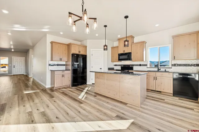 a kitchen with stainless steel appliances kitchen island granite countertop a stove a sink a refrigerator and white cabinets with wooden floor