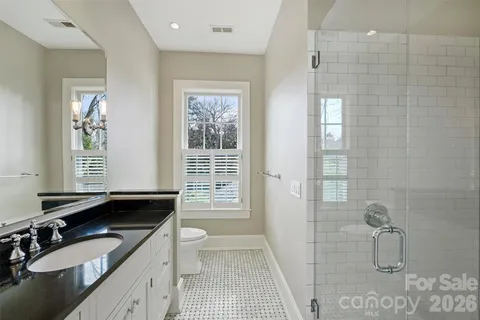 a bathroom with a granite countertop sink a toilet a mirror and a shower