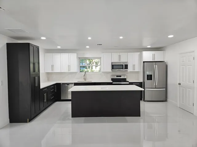 a large kitchen with stainless steel appliances kitchen island granite countertop a refrigerator and a stove top oven