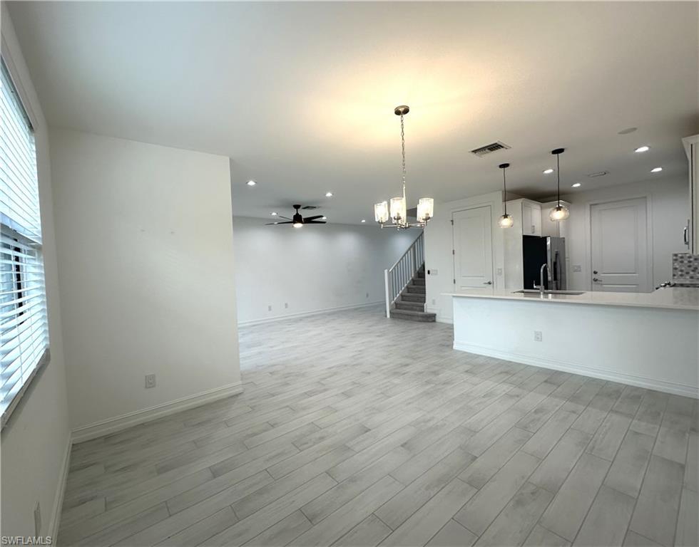 7509 Carnegie Way Naples, FL 34119 - Photo 4 of 33 an empty room with wooden floor and a kitchen