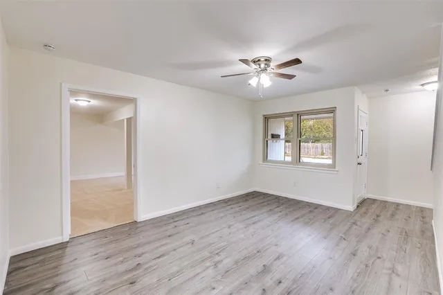 an empty room with wooden floor ceiling fan and windows