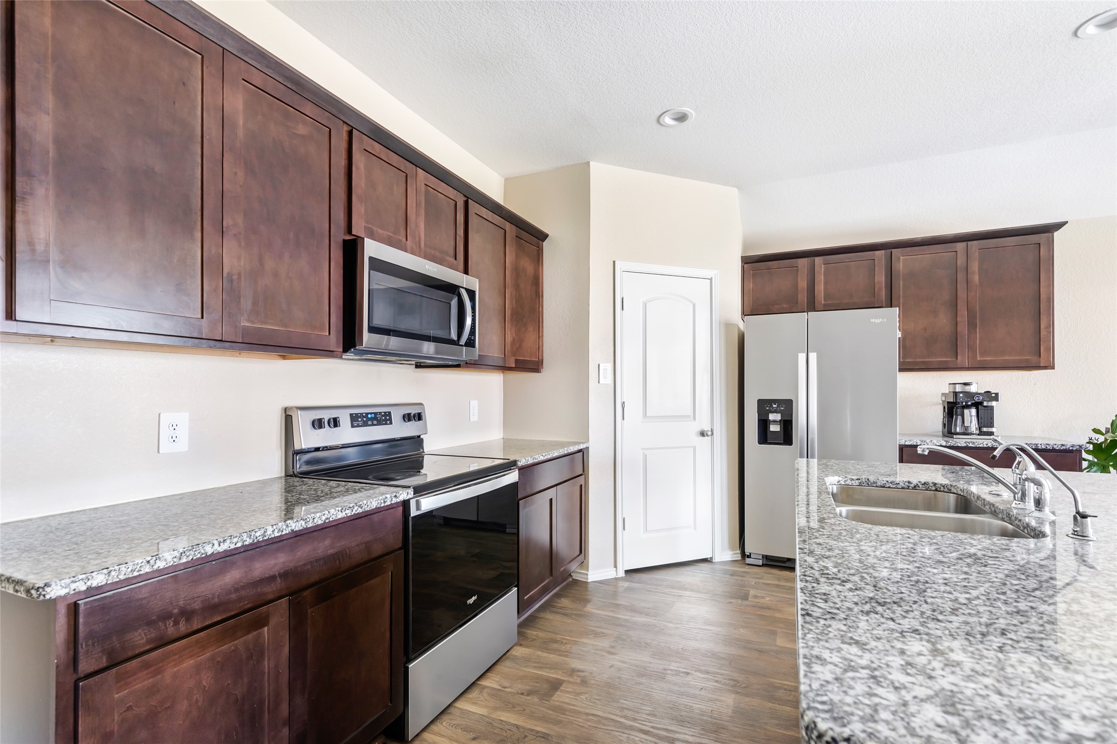 811 Republic Road New Caney, TX 77357 - Photo 24 of 37 This modern kitchen features sleek granite countertops, dark wood cabinets, and stainless steel appliances, including a built-in microwave. The open layout and light wood like flooring create a spacious and inviting atmosphere, perfect for cooking and entertaining.