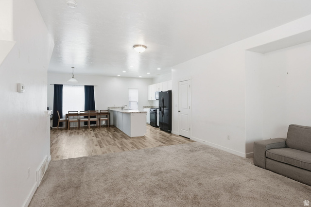 14764 Rising Star Way Riverton, UT 84065 - Photo 7 of 42 Open-concept living space featuring carpeted and wood-finish flooring, a kitchen island with a stone-finish countertop, and recessed lighting
