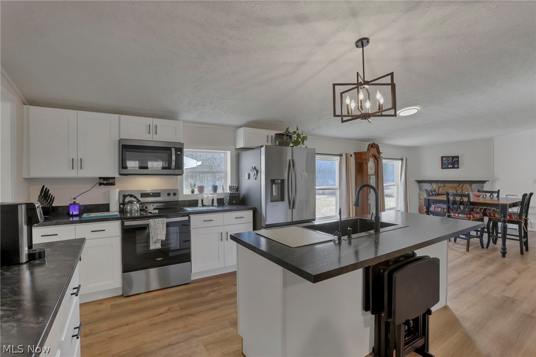 3750 Cannelville Road Roseville, OH 43777 - Photo 6 of 33 Kitchen with stainless steel appliances, dark countertops, a kitchen island with sink, light wood-style floors, and white cabinetry