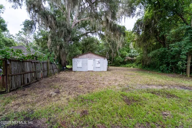 a backyard of a house with large trees and wooden fence