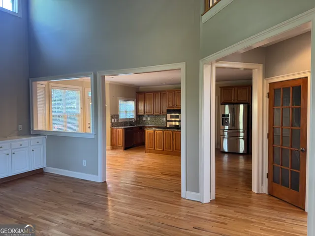 an empty room with wooden floor and way to kitchen