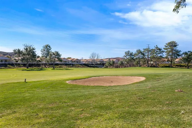 a view of a large pool with lawn chairs and big trees