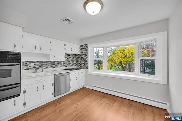 a kitchen with stainless steel appliances granite countertop a stove a sink and white cabinets with wooden floor