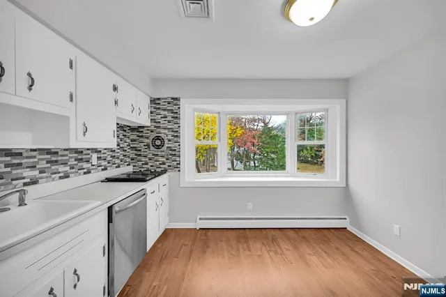 a kitchen with granite countertop a stove a sink and white cabinets with wooden floor