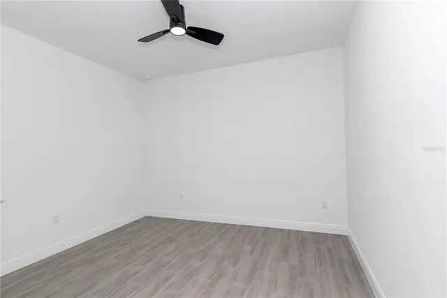 an empty room with wooden floor ceiling fan and windows