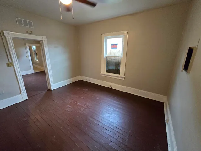 an empty room with wooden floor fan and window