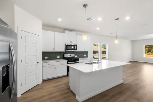 a kitchen with stainless steel appliances granite countertop a refrigerator a sink dishwasher a oven and a dining table with wooden floor