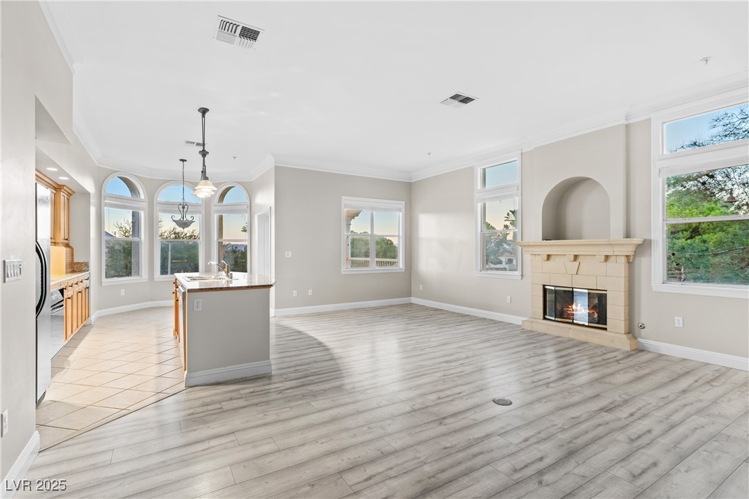 35 Strada Di Circolo Henderson, NV 89011 - Photo 5 of 28 Unfurnished living room with crown molding, a fireplace, plenty of natural light, light wood-type flooring, and a chandelier
