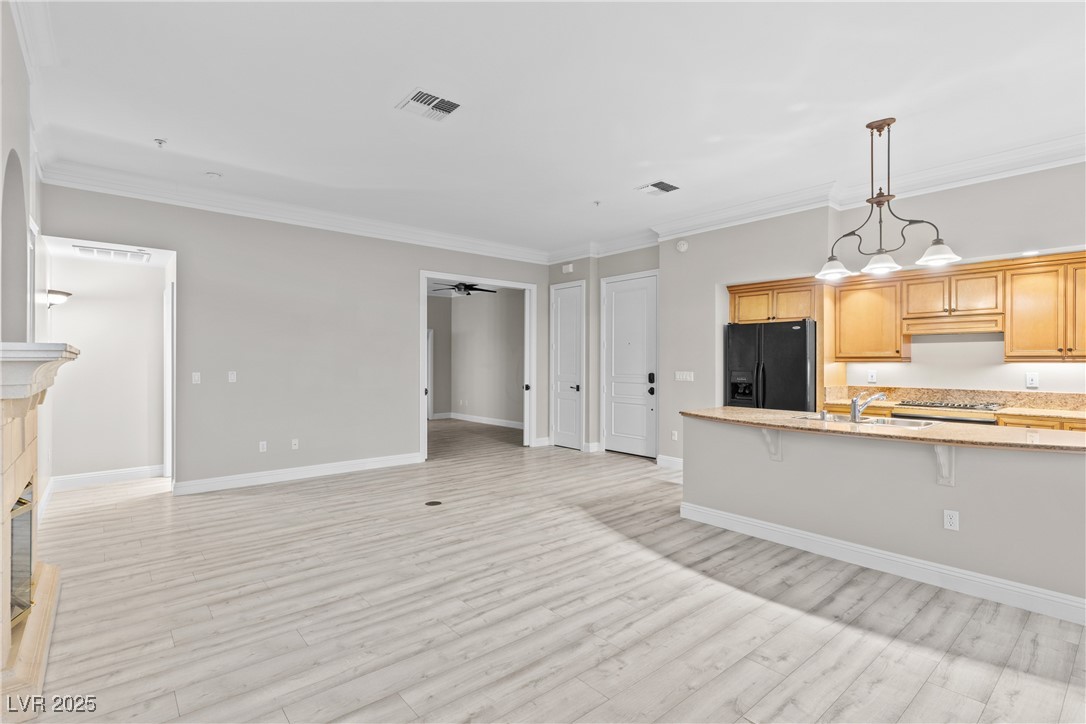 35 Strada Di Circolo Henderson, NV 89011 - Photo 10 of 28 Kitchen with ornamental molding, black fridge, a kitchen bar, hanging light fixtures, and light wood finished floors