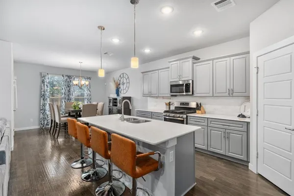 a kitchen with stainless steel appliances granite countertop a stove a refrigerator a kitchen island a sink white cabinets and couches with wooden floor