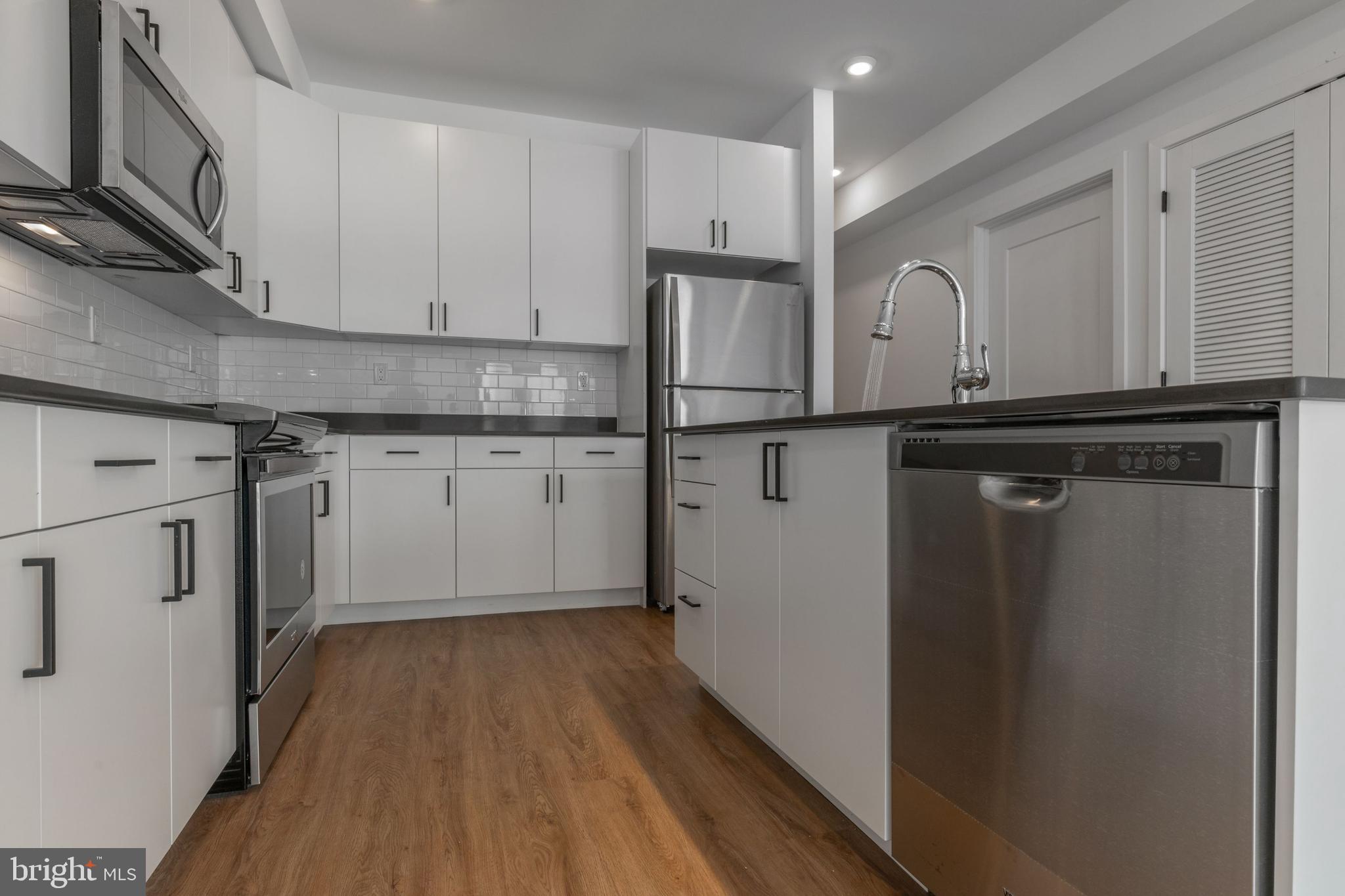 a kitchen with stainless steel appliances granite countertop a refrigerator a sink and white cabinets with wooden floor