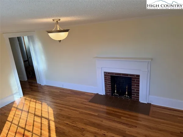 a view of an empty room with wooden floor and a fireplace