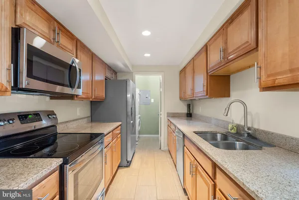 a kitchen with stainless steel appliances granite countertop a sink a stove top oven a refrigerator cabinets and a kitchen island