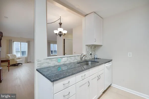 a kitchen with stainless steel appliances granite countertop a sink dishwasher and white cabinets with wooden floor