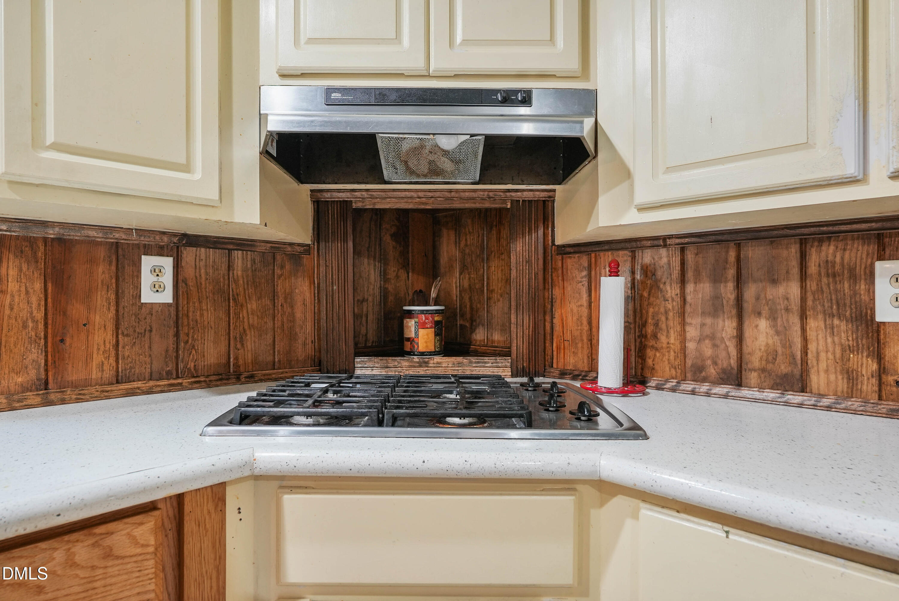 7406 Old Beulah Road Kenly, NC 27542 - Photo 12 of 30 Corner kitchen counter with an integrated gas cooktop, white solid surface countertop, wood-paneled backsplash, cream-painted upper and lower cabinetry, and a stainless steel range hood