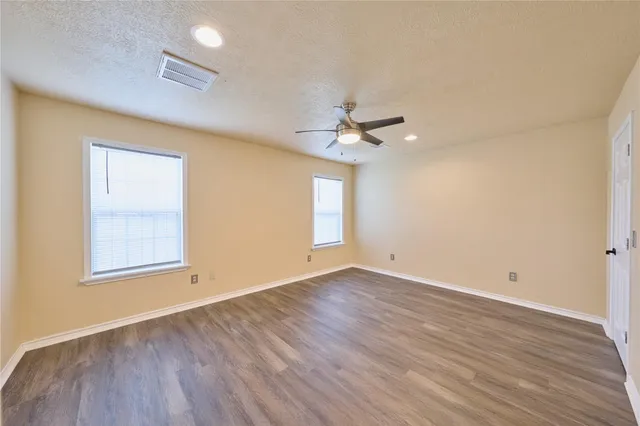 an empty room with wooden floor chandelier fan and windows