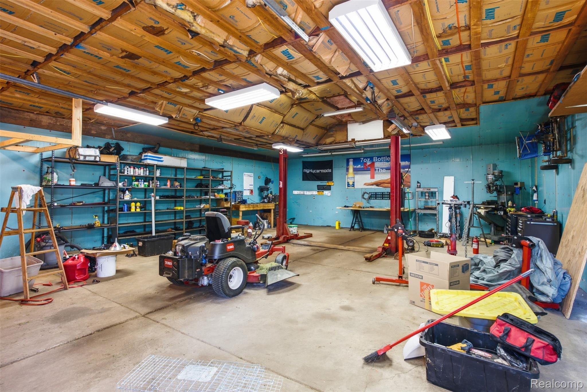 9200 Hickory Ridge Road Holly, MI 48442 - Photo 32 of 33 Spacious garage featuring a concrete floor, exposed wood beam ceiling, ample fluorescent lighting, and extensive shelving for storage