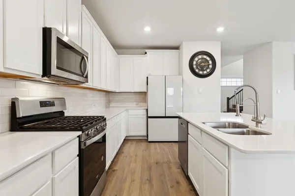 a kitchen with stainless steel appliances granite countertop a sink a stove top oven a clock and cabinets