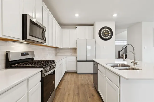 a kitchen with stainless steel appliances granite countertop a sink a stove top oven a clock and cabinets