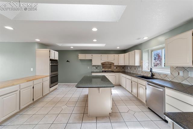 3240 Spaatz Road Monument, CO 80132 - Photo 17 of 45 Kitchen with a kitchen island, backsplash, appliances with stainless steel finishes, sink, and light tile floors