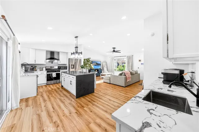 a kitchen with stainless steel appliances kitchen island granite countertop a stove top oven a sink dishwasher a dining table and chairs with wooden floor