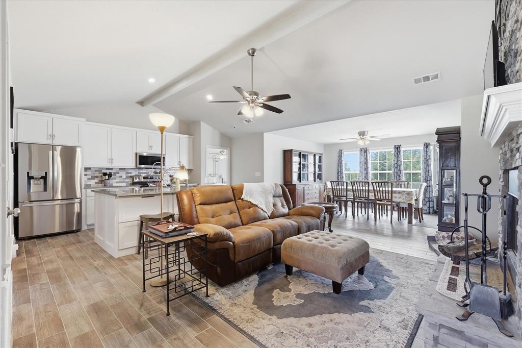 110 Highview Road Ennis, TX 75119 - Photo 7 of 40 Open concept living space featuring wood-finish flooring, a stone fireplace, and a kitchen with white cabinetry and stainless steel appliances
