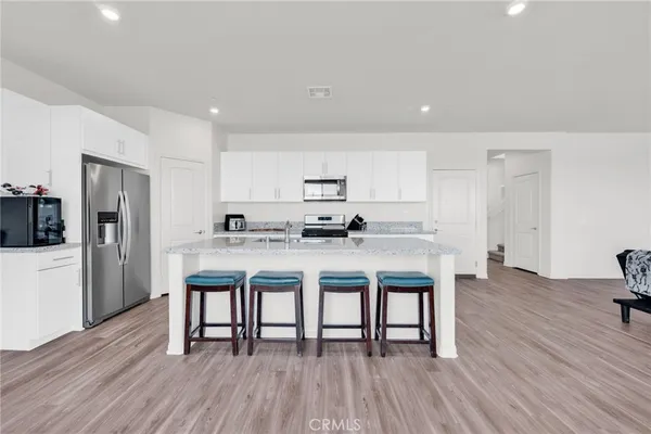 a kitchen with stainless steel appliances granite countertop a refrigerator a stove a sink a dining table and chairs with wooden floor