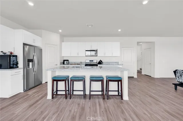 a kitchen with stainless steel appliances granite countertop a refrigerator a stove a sink a dining table and chairs with wooden floor