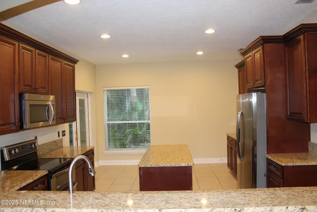 a kitchen with stainless steel appliances granite countertop a refrigerator a stove and a sink with wooden cabinets
