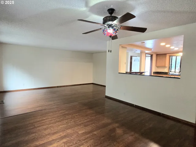 an empty room with wooden floor chandelier fan and windows