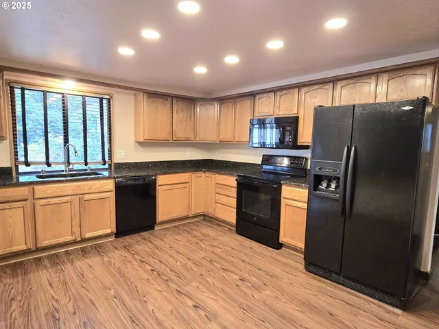 a kitchen with stainless steel appliances granite countertop a refrigerator a sink dishwasher a stove and white countertops with wooden floor