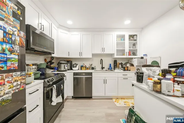 a kitchen with stainless steel appliances granite countertop a stove top oven a sink dishwasher and white cabinets with wooden floor