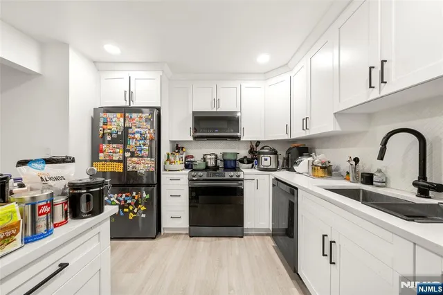 a kitchen with stainless steel appliances granite countertop a stove top oven a sink dishwasher and white cabinets with wooden floor