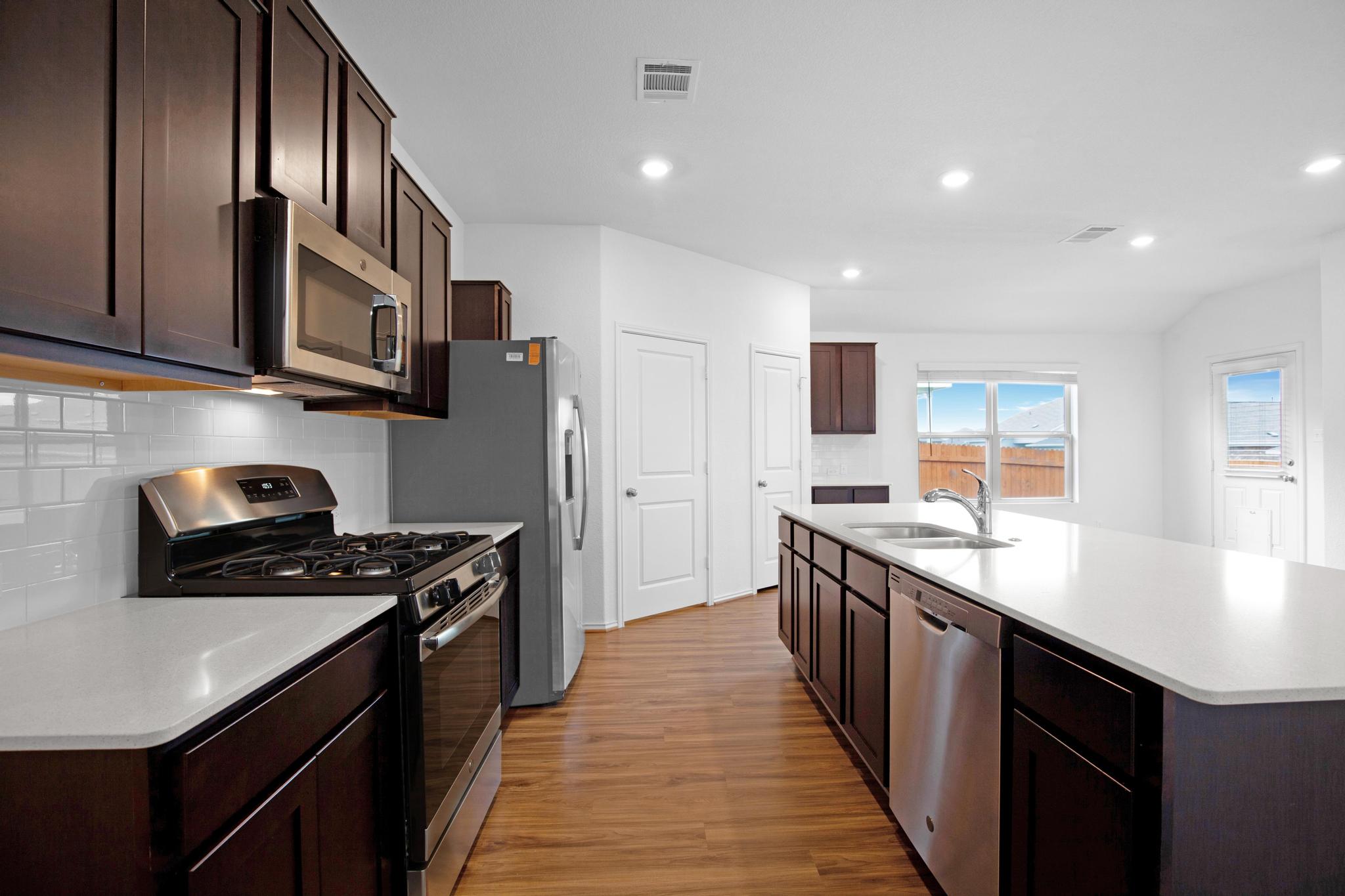 21409 Resource Road Pflugerville, TX 78660 - Photo 5 of 23 Kitchen featuring stainless steel appliances, dark wood finish cabinetry, a kitchen island with sink, dark wood finished floors, and tasteful backsplash