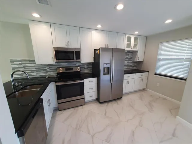 a kitchen with stainless steel appliances granite countertop a refrigerator a stove a sink and a microwave