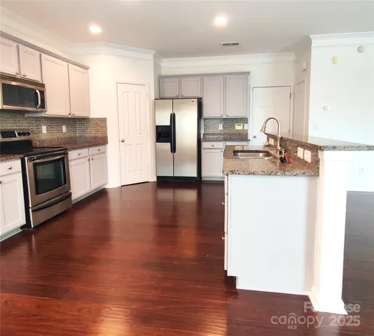 a kitchen with stainless steel appliances granite countertop a refrigerator a stove top oven a sink and dishwasher with wooden floor