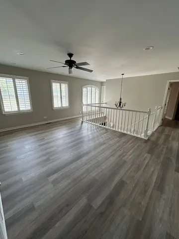 an empty room with wooden floor chandelier and windows