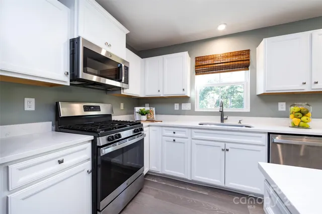 a kitchen with stainless steel appliances granite countertop white cabinets a sink and a window