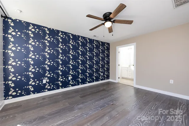 a view of an empty room with wooden floor and a ceiling fan