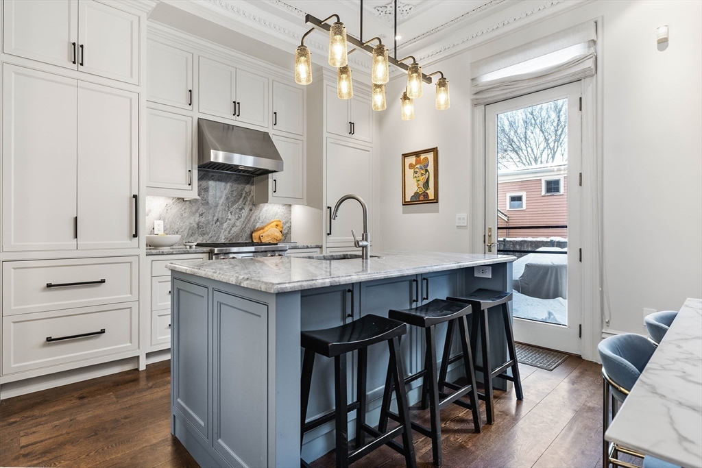 93 Third Street, Unit 93 Cambridge, MA 02141 - Photo 11 of 42 a kitchen with kitchen island granite countertop a table chairs refrigerator and microwave