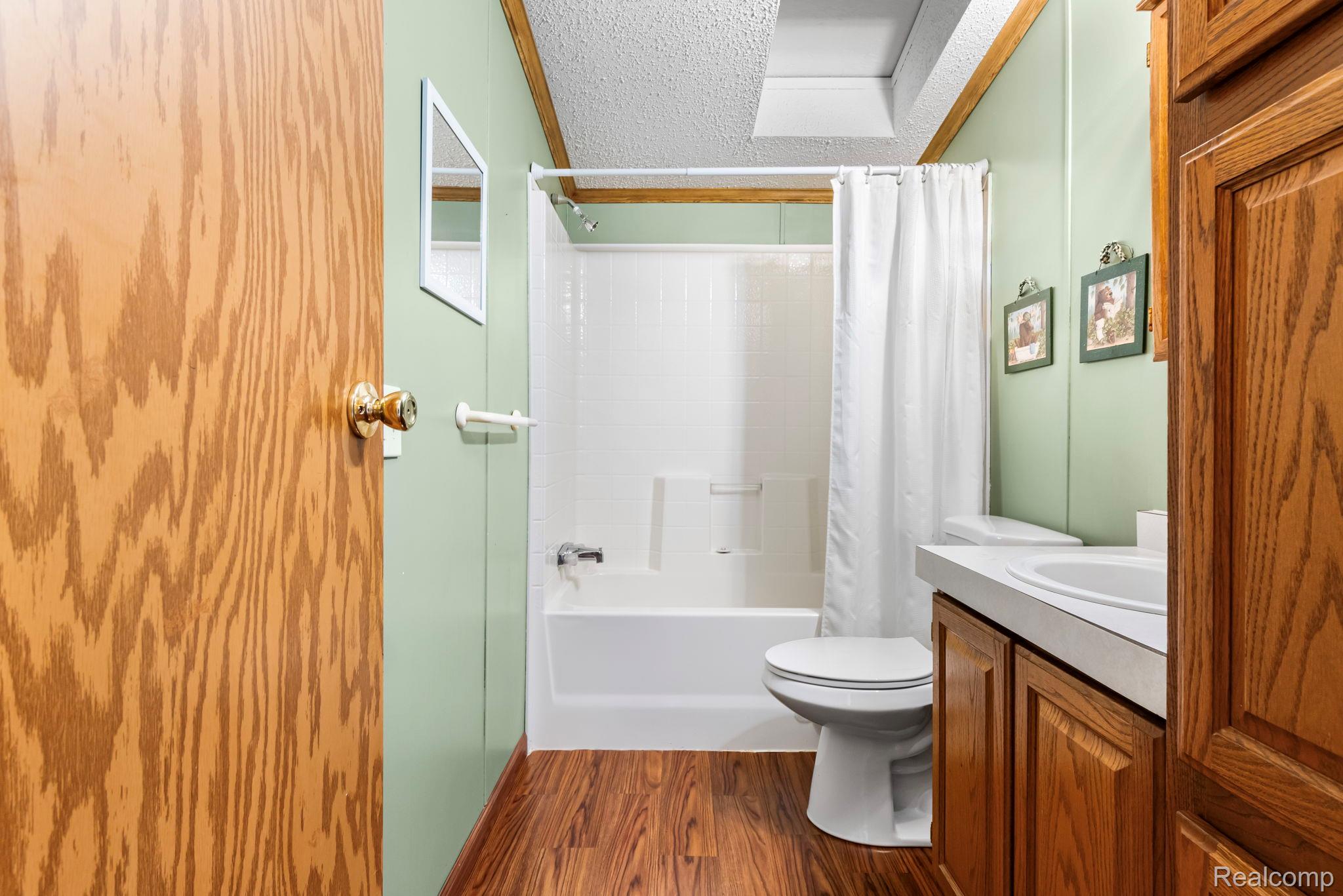 4884 Griffin Road Lewiston, MI 49756 - Photo 23 of 41 Bathroom featuring wood-finish flooring, a white bathtub with a shower, a toilet, a vanity with a built-in sink, and wood cabinetry
